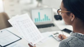 An employee sits at the computer with spreadsheets.